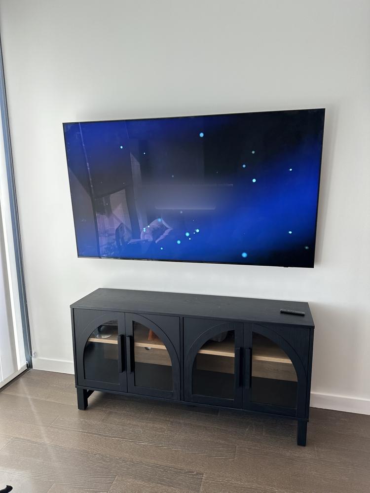 Large Samsung TV on a full-motion mount folded flat to the wall above a black media console