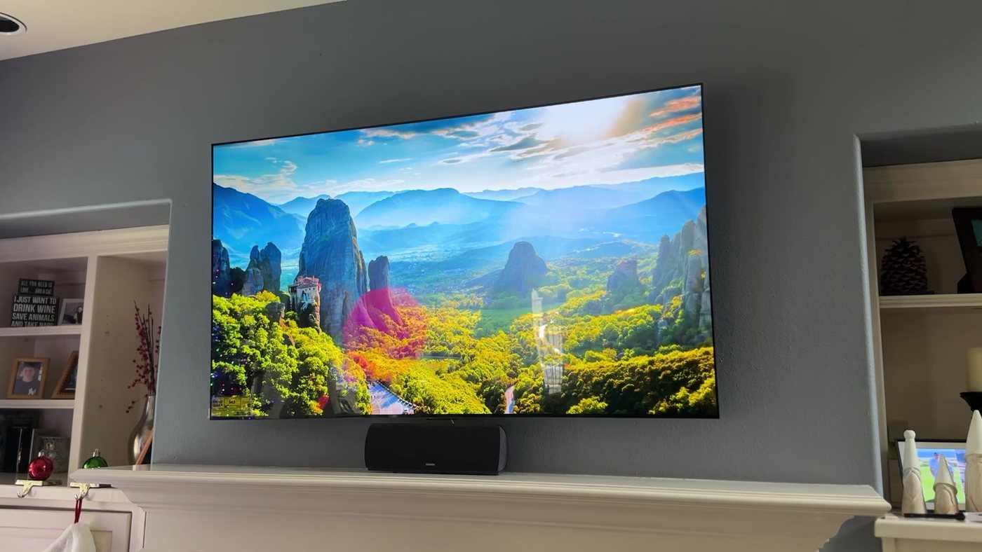 Large TV mounted over a white fireplace mantel with a center speaker below