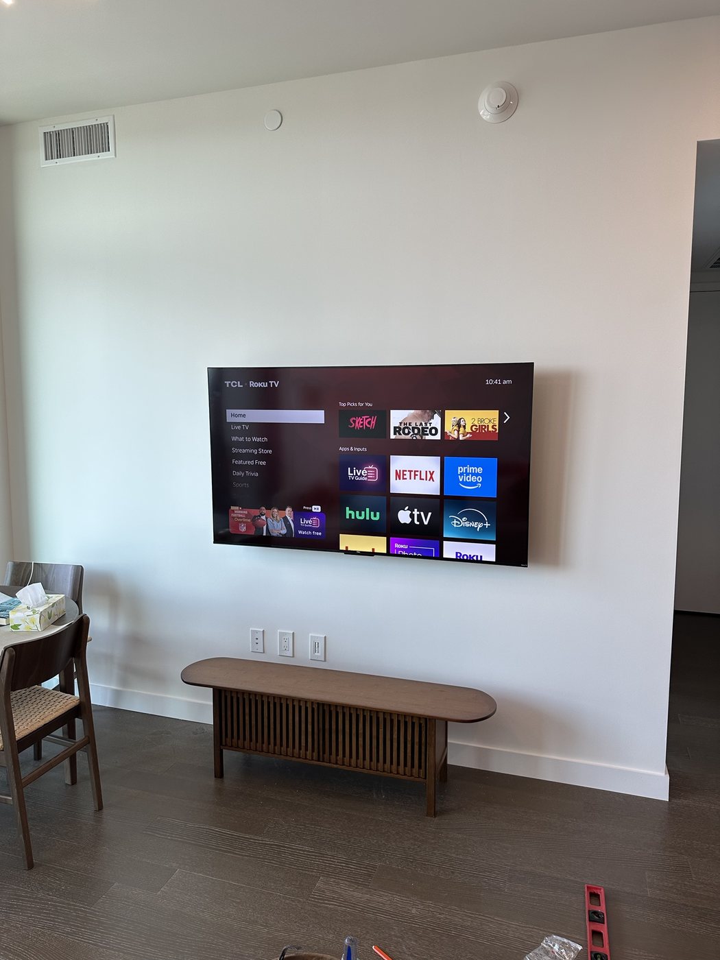 TCL TV with a Roku streaming device on a bench below